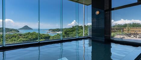 A modern indoor swimming pool with large windows offering a view of a tropical island and ocean.