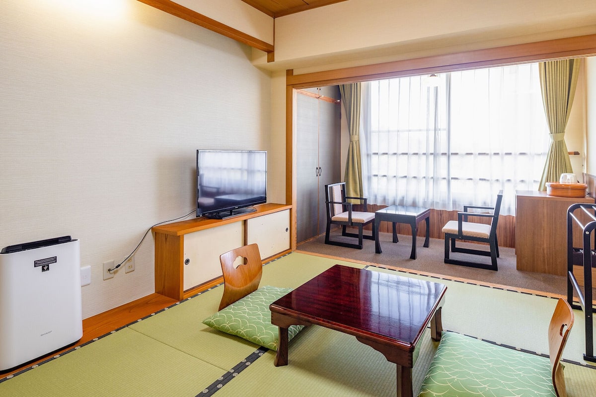 A traditional Japanese room with tatami flooring, a television, a wooden table, and a sofa.