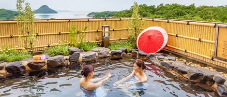 A traditional Japanese onsen with a bamboo fence, a wooden bench, and a red umbrella.