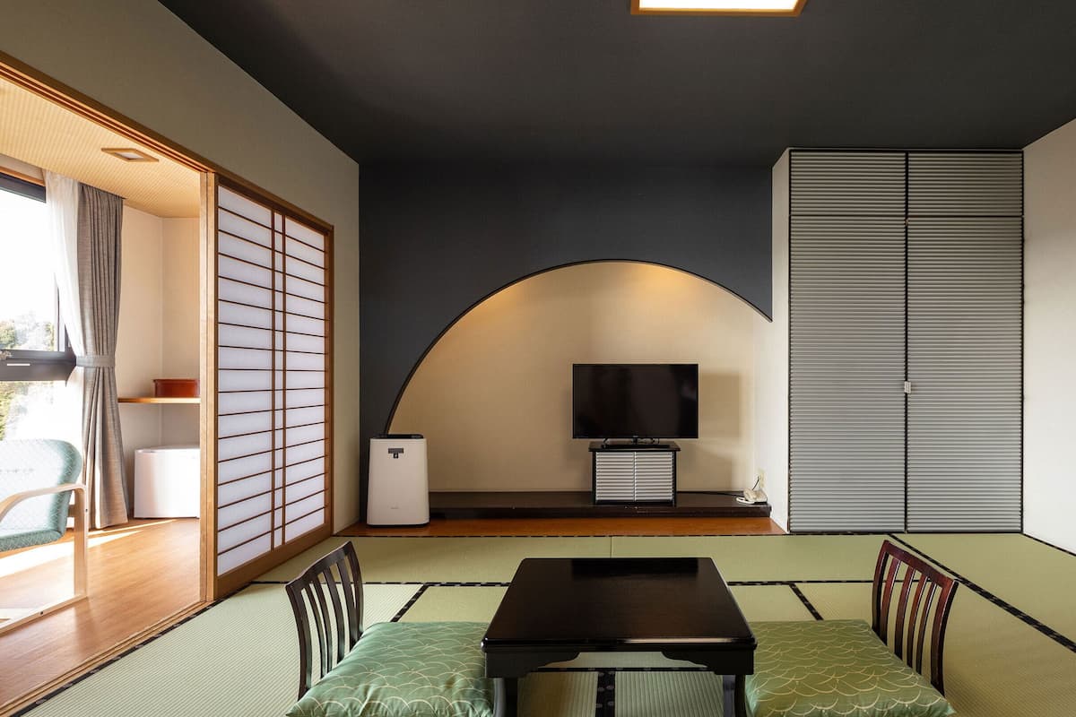 A traditional Japanese room with tatami flooring, a low table, a television, and sliding doors.