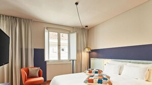 Ein Hotelzimmer mit Bett, Stuhl, Lampe und Fenster.