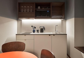 Une cuisine compacte équipée d’un four à micro-ondes, d’une machine à café et d’ustensiles de cuisine, le tout placé sur le plan de travail.