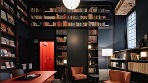 A library with bookshelves, a red door, and seating areas. - Studio - Urbanauts Studios Minelli (Trieste)