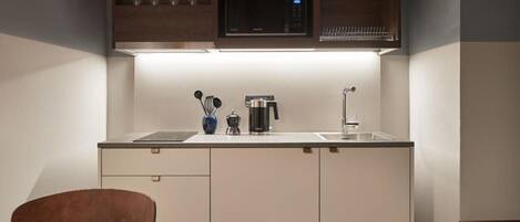 A compact kitchen with a microwave, coffee maker, and utensils on the counter.