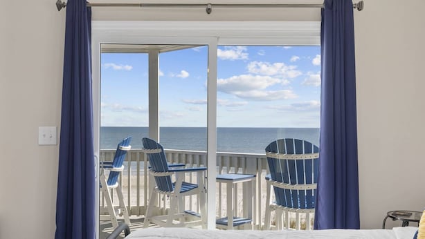 Quarto com cama, varanda com cadeiras e vista para o mar.