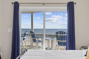 Une chambre avec un lit, un balcon avec des chaises et une vue sur la mer.