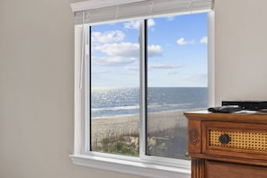Ein Zimmer mit großem Fenster und Blick auf einen Strand.