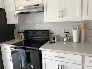 A kitchen with white cabinets, a black stove, and a tiled backsplash.