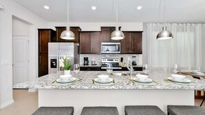 Une cuisine moderne dotée de plans de travail en granit, de meubles en bois foncé, d’appareils électroménagers en acier inoxydable et de luminaires suspendus.