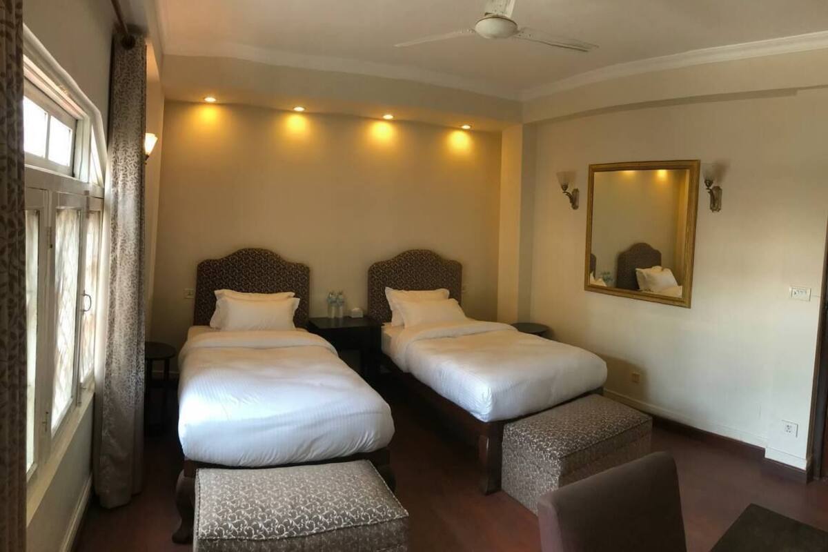 Habitación de hotel con dos camas, un ventilador de techo, un espejo grande y una ventana con cortinas.