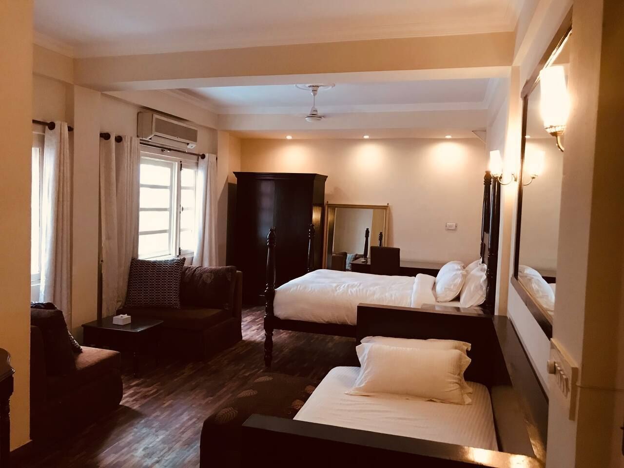 A hotel room with two beds, a sofa, a desk, and a mirror.