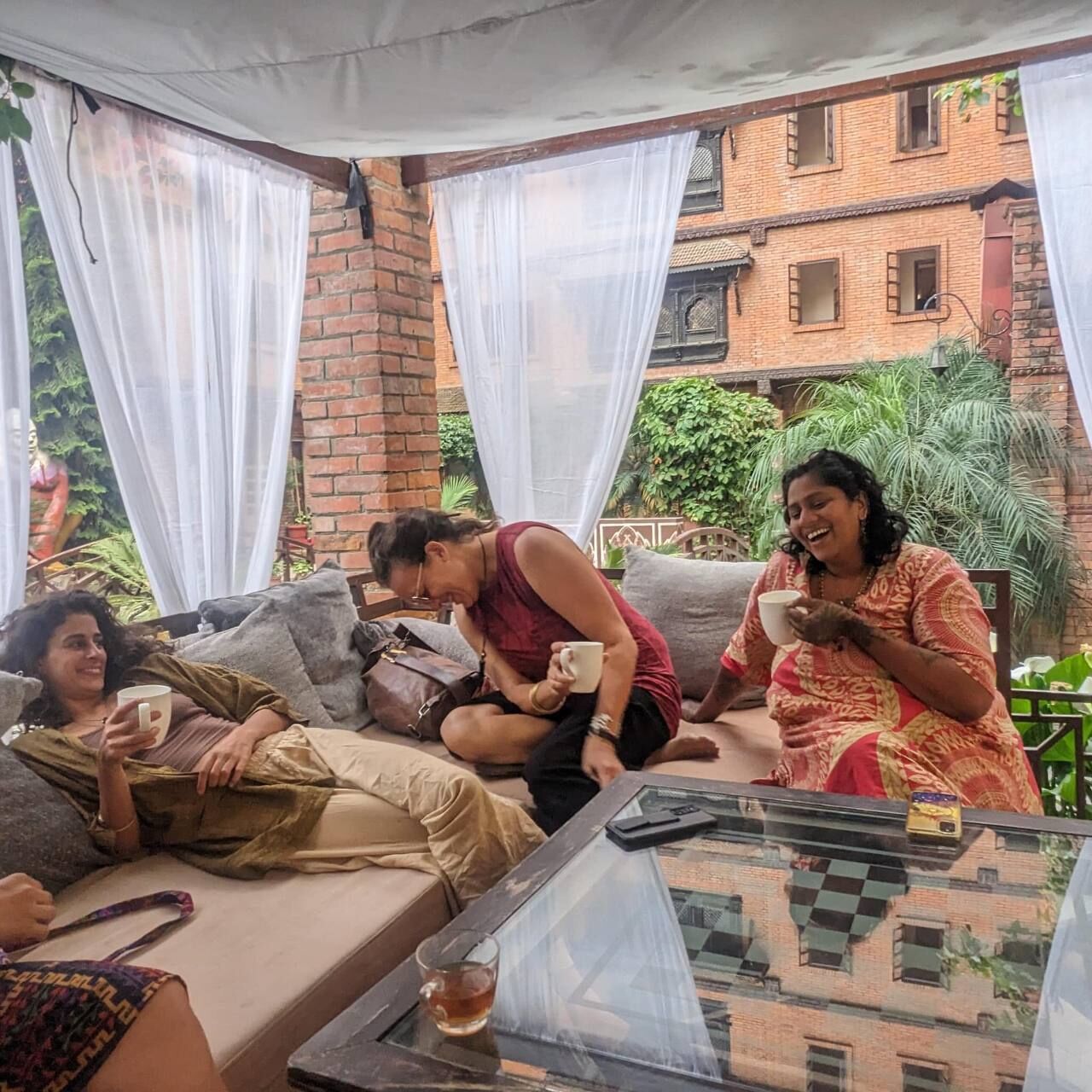 A group of people sitting on a sofa and chairs in an outdoor setting with a glass table in front.