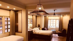 A hotel room with two single beds, a sitting area with a sofa and armchairs, a dining table, and a large window with curtains. - Courtyard Pujan Hotel (Kathmandu)