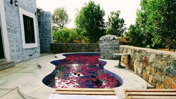 Piscina com vitórias-regias, rodeada por paredes de pedra e espreguiçadeiras de madeira.