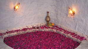 Uma área circular de mármore com pétalas de rosa e um vaso de latão com frutas e uma flor.