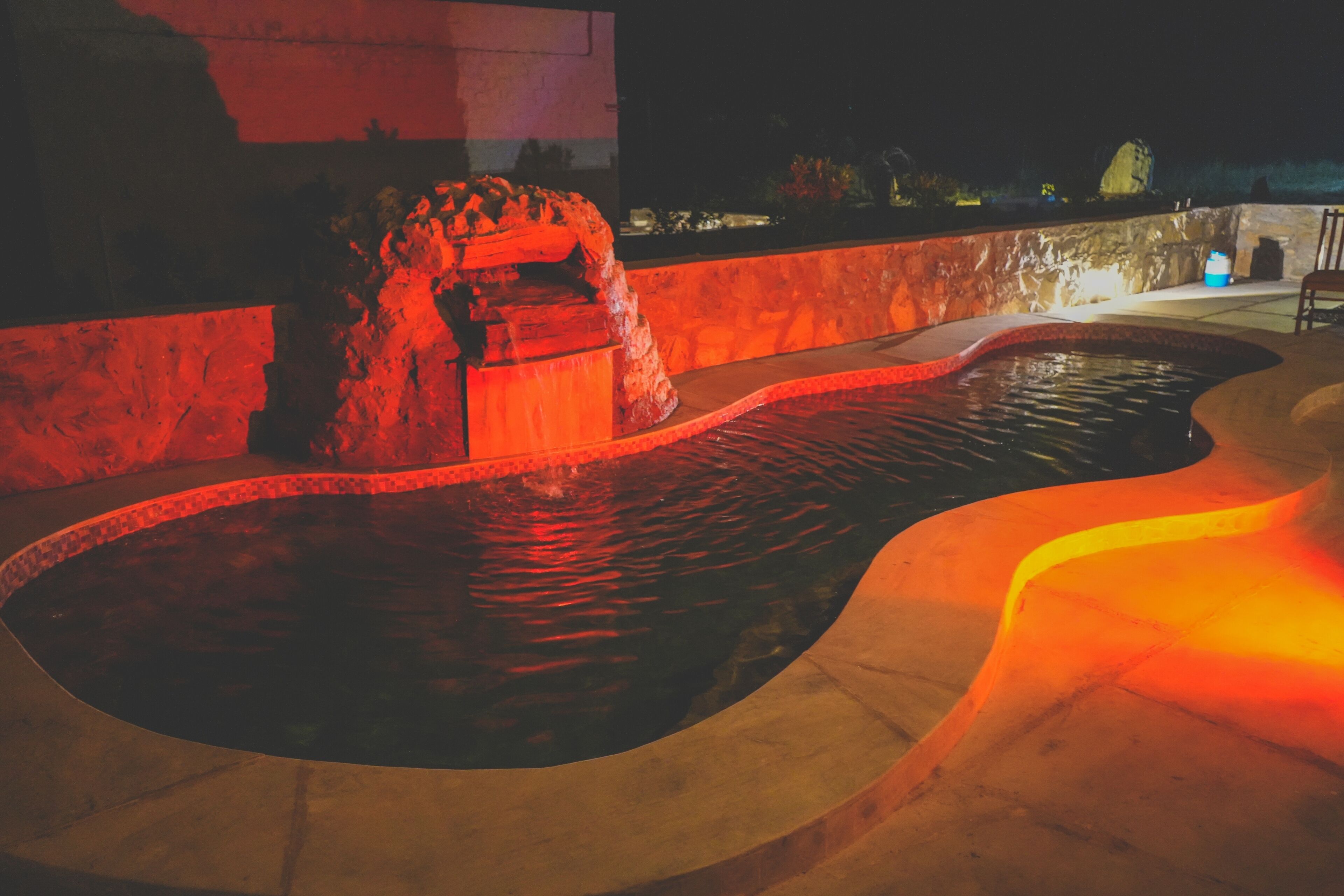 A swimming pool with a stone structure and a curved edge, surrounded by a stone wall and a wooden deck.