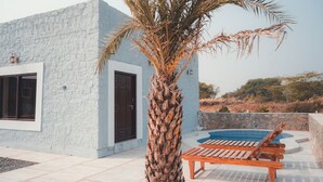 Um edifício moderno com fachada de pedra, uma palmeira e área de piscina com espreguiçadeiras.