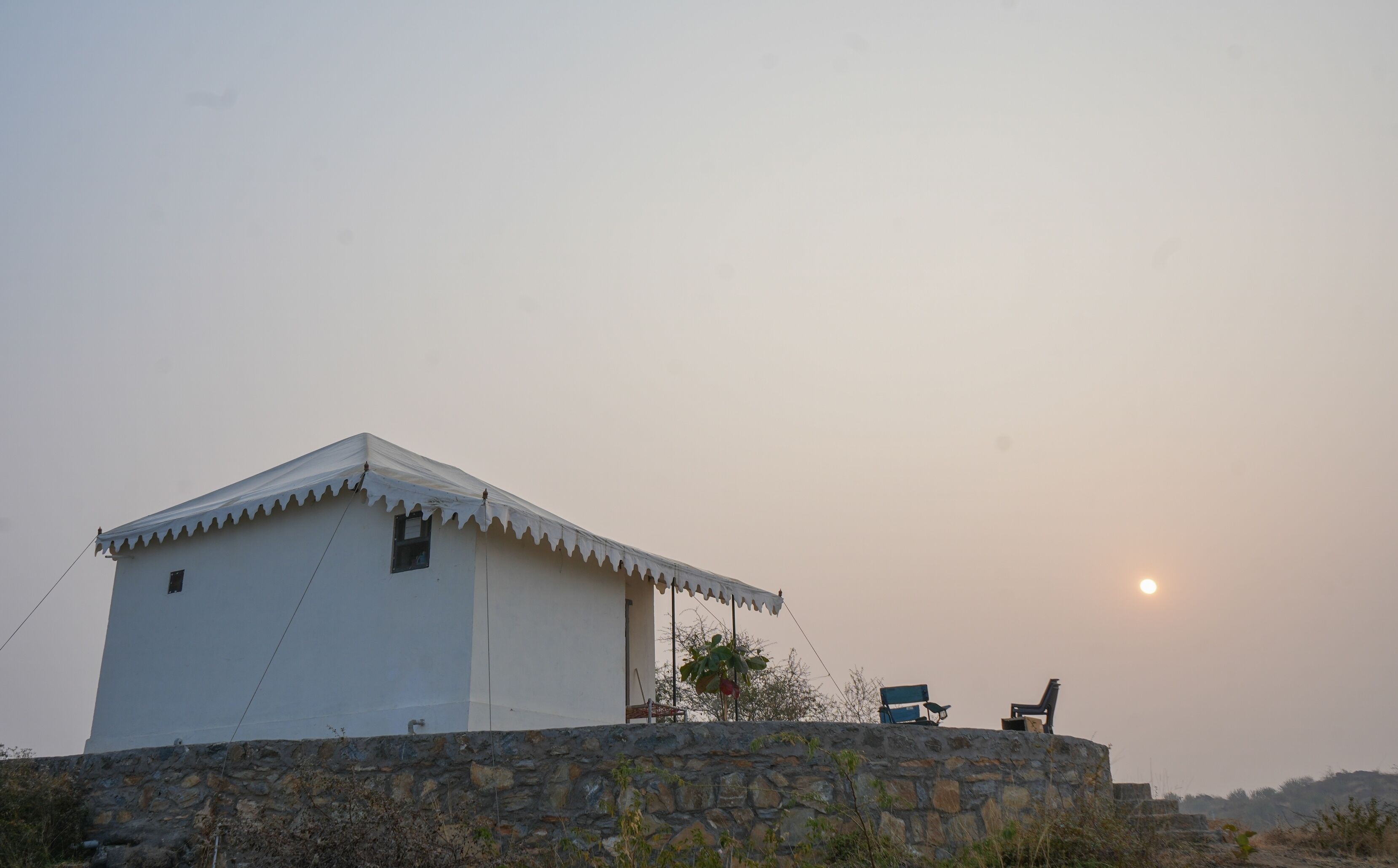 A white building with a stone wall foundation, a small window, and a flat roof.