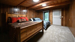 A wooden cabin bedroom with a large bed, a smaller bed, and a door leading outside.