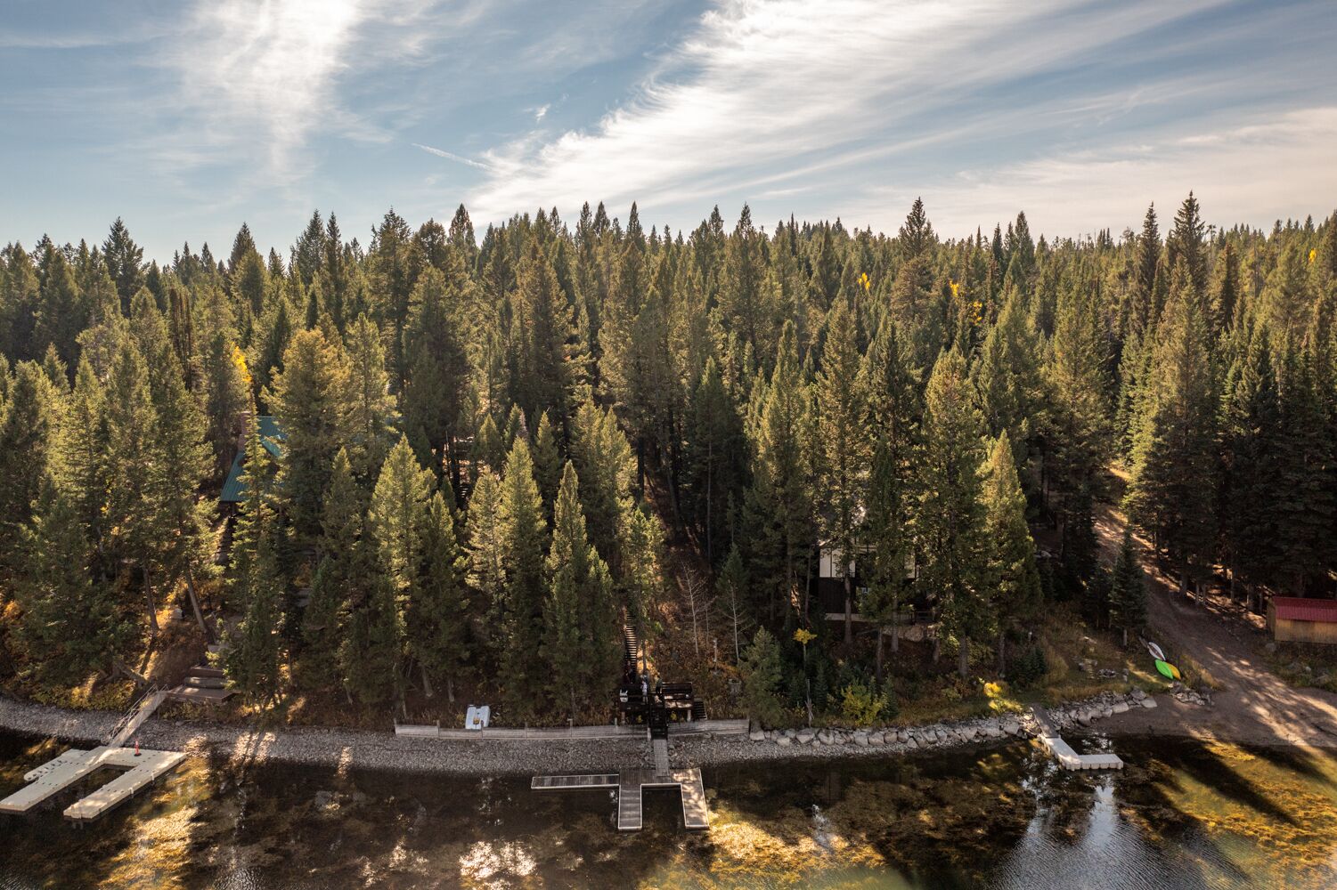 An aerial view of a forested area with a dock extending into a body of water, surrounded by dense trees.