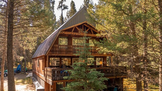 A rustic cabin with a wooden exterior, a balcony, and a covered porch area surrounded by trees.