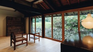 Um quarto espaçoso com piso de madeira, uma grande janela com vista para uma parede de pedra e teto de madeira.