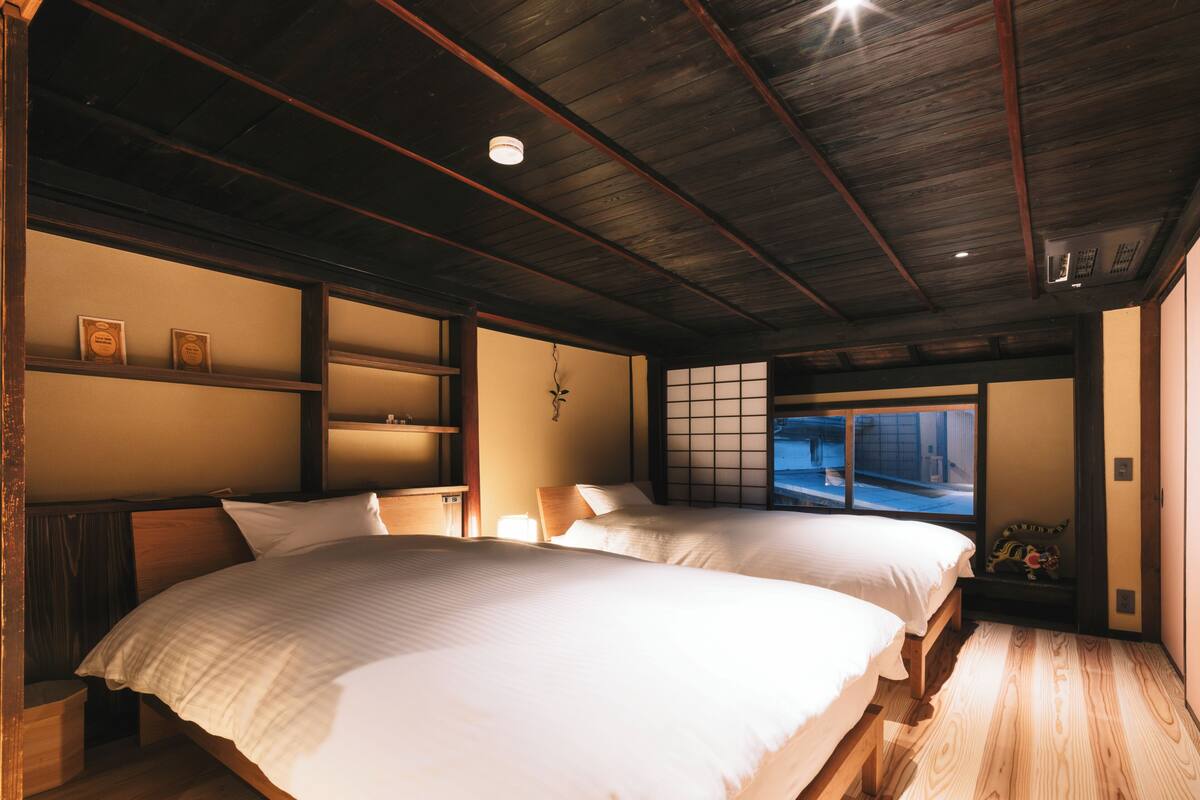 Une pièce de style japonais traditionnel, dotée de deux lits, d’un plancher en bois et d’une porte coulissante donnant sur l’extérieur.