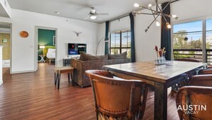 A spacious living area with a wooden dining table, leather chairs, a large window with a view, a ceiling fan, and a flat-screen TV. - TNC #205 xxxxxxxxxxx (Austin)