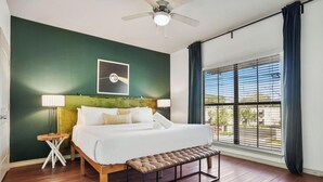 A bedroom with a bed, a bench, a nightstand, a ceiling fan, a window with blinds, and a wall with a framed picture. - TNC #205 xxxxxxxxxxx (Austin)