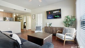A modern living room with a flat-screen TV displaying various streaming services, a wooden coffee table, and comfortable seating. - TNC #206 xxxxxxxxxxx (Austin)