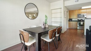 A modern kitchen with stainless steel appliances, a dining area with a dark table and wooden chairs, and a cactus plant on the wall. - TNC #206 xxxxxxxxxxx (Austin)