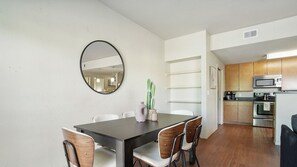 A modern kitchen with stainless steel appliances, a dining area with a dark table and wooden chairs, and a cactus plant on the wall.