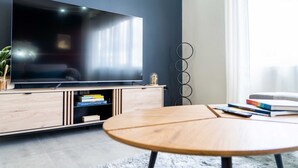 A modern living room with a flat-screen TV on a wooden TV stand, a round wooden coffee table, and a bookshelf with books. - Modern 3BR Home with Own Private Pool - Centrally Located - Quiet Neighborhood (Cole bay)