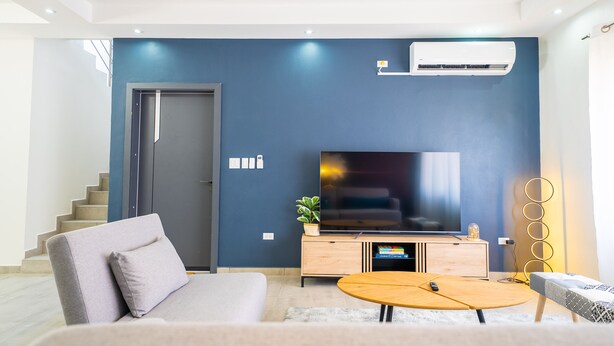 A modern living room with a sofa, a coffee table, a TV, and a staircase. - Modern 3BR Home with Own Private Pool - Centrally Located - Quiet Neighborhood (Cole bay)