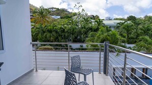 A balcony with two metal chairs, a metal railing, and a view of lush greenery and buildings in the background. - Modern 3BR Home with Own Private Pool - Centrally Located - Quiet Neighborhood (Cole bay)