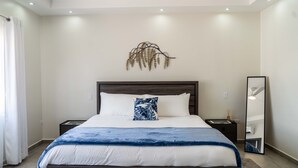 A modern bedroom with a large bed, a nightstand, a mirror, and a wall-mounted light fixture. - Modern 3BR Home with Own Private Pool - Centrally Located - Quiet Neighborhood (Cole bay)