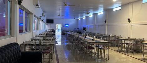 A spacious dining area with multiple tables and chairs, ceiling fans, and large windows.