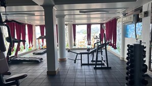 A gym with exercise equipment, large windows, and a view of greenery. - AT Hotels & Resorts (Port Blair)