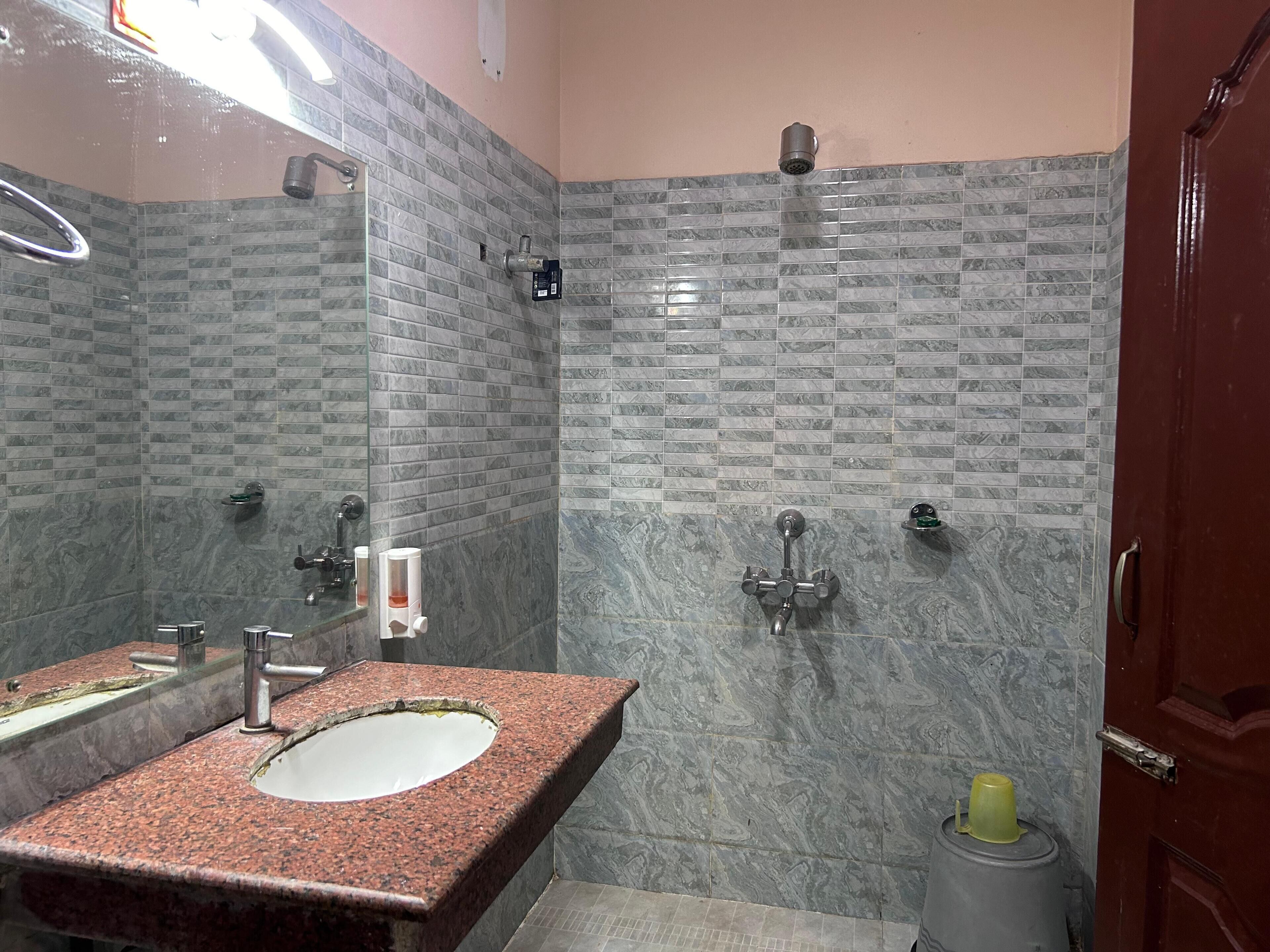 Un baño con lavamanos de encimera de granito, un espejo, ducha con cabezal de ducha manual y un inodoro.