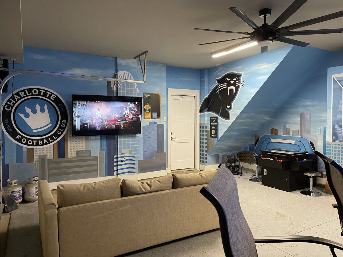 Una habitación con televisor grande, un sofá, ventilador de techo y un mural en la pared.