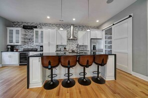 A modern kitchen with white cabinets, a central island with bar stools, and a backsplash with a mosaic pattern.