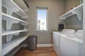 A laundry room with white shelving, a window, a washing machine, and a trash can. - 906 Westbrook B  · City Views RoofTop & Short Walk to Stadium (Charlotte)