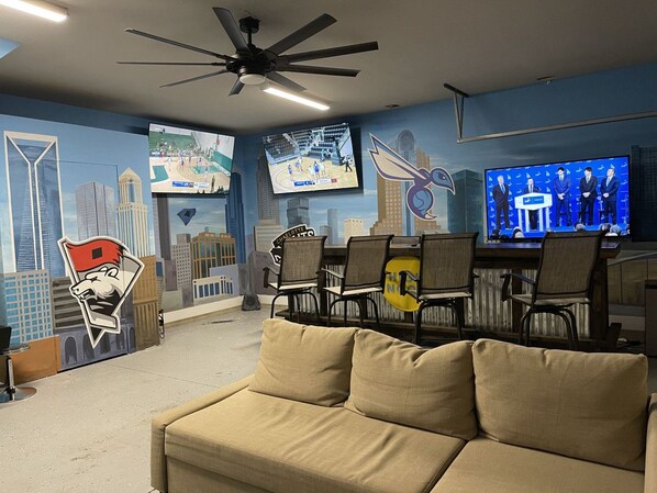 A room with a beige sofa, a TV mounted on the wall, and a cityscape mural.