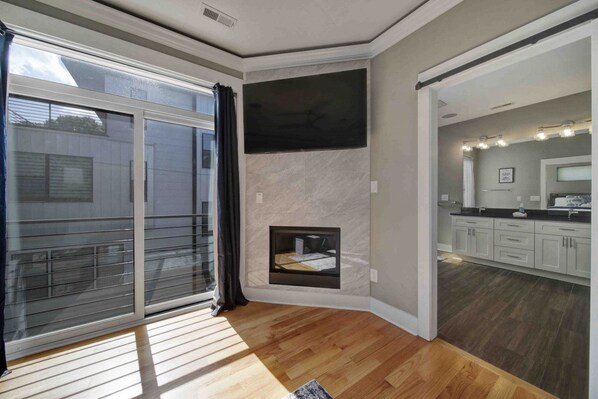 Una sala de estar moderna con chimenea, un televisor grande y un ventanal corredera que da a un balcón.