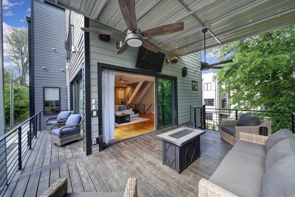 A modern house with a wooden deck, outdoor seating, and a large sliding door leading to an interior space.