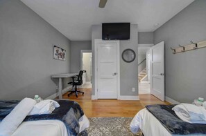 Une chambre avec deux lits, un bureau, une chaise, une télévision et un escalier menant à une autre pièce.