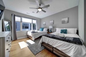 A modern bedroom with two beds, a ceiling fan, large windows, and a wooden dresser. - 906 Westbrook B  · City Views RoofTop Hot Tub & Short Walk to Stadium (Charlotte)