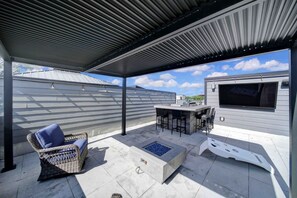Un patio exterior con zona de estar cubierta, una chimenea y una barra.