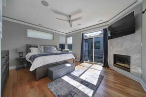 A modern bedroom with a bed, a ceiling fan, a fireplace, and a large window. - 906 Westbrook B  · City Views RoofTop & Short Walk to Stadium (Charlotte)