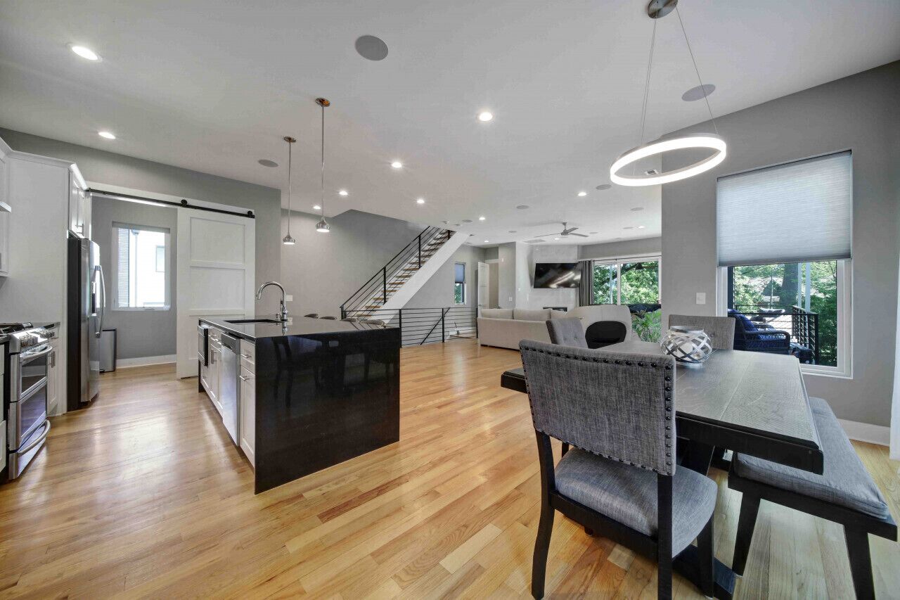 A modern kitchen with a central island, a dining area with a table and chairs, and a staircase leading to an upper level.